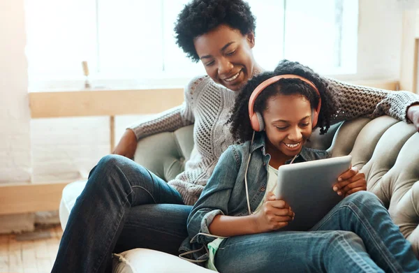 Black family, headphones and tablet to listen to music, streaming and online learning on lounge sofa. Woman or mother and teenager together in living room while happy about home wifi for education.