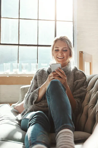 Woman, sofa and phone with smile, chat and communication on internet to relax in lounge. Girl, couch and texting on social network, mobile tech or streaming video for comedy, meme and happy in house.