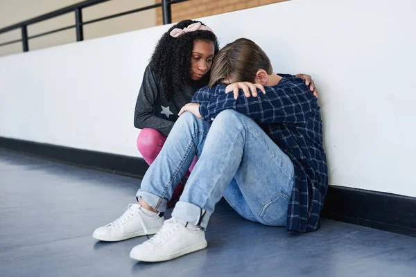 Are you okay. Full length shot of an unrecognizable boy sitting in the school hallway and feeling depressed while a classmate comforts him