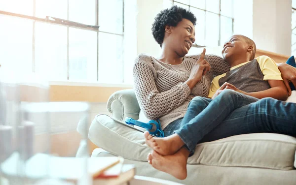 Black family, son and mother relax on a sofa, laugh and happy while bond in their home together. Mom, love and boy resting with parent, content and playful while sitting and talking in living room.