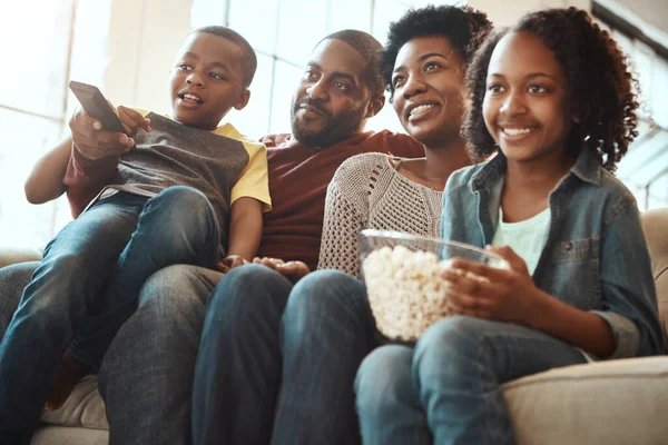 Black family watching tv on sofa for movie, film and cartoon together, bonding and quality time in living room. Popcorn, kids television show of people, mother and father with kids, on couch watching.