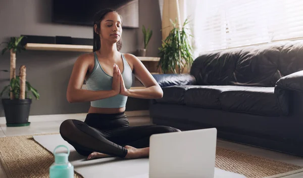 meditation is a great way to start your day. a young woman following a yoga routine using her laptop at home