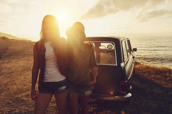 Sunset lens flare with women, car and road trip, travel with friends at beach, outdoor with nature and sea holiday. Transportation, freedom and sunshine on summer vacation, happiness with adventure.