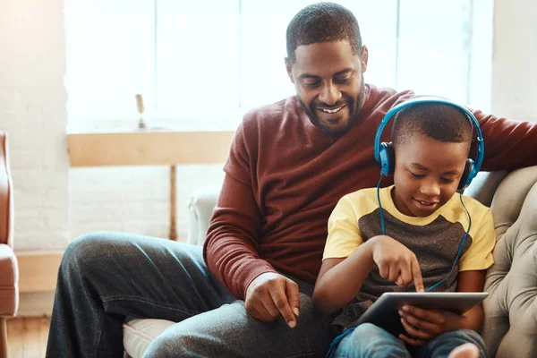 Tablet, happy and dad with his son on a sofa watching a funny, comic or meme video on social media. Relax, smile and African man streaming a movie with child on mobile device while relaxing together