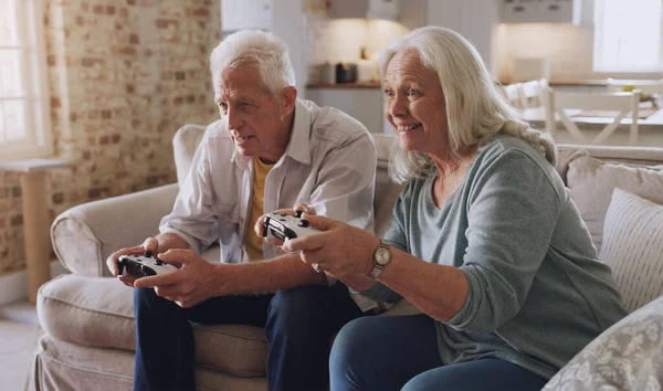 Giving these youngsters a run for their money. a senior couple sitting on the sofa at home together and gaming