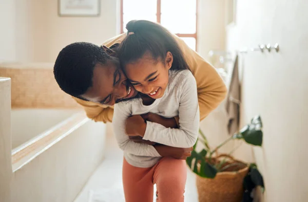 Black family, father and child for a hug in happy home with love, care and support in bathroom. Man and girl kid together for happiness with smile, energy and embrace for safety, health and wellness.
