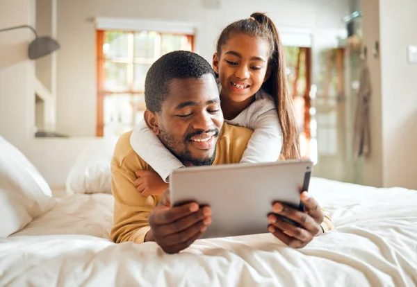 Black family, tablet or education with a father and daughter lying together on a bed in their home for learning. Relax, internet and kids with a man and girl in a bedroom for growth or development.