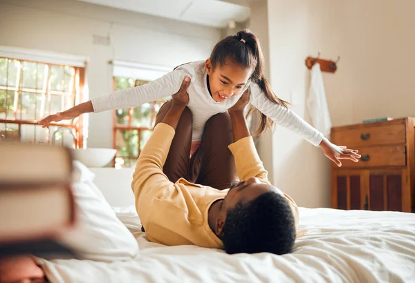 Father, child and playing on bed flying for fun quality bonding time together indoors at home. Happy dad holding daughter in air with knees and arms in bedroom for playful relationship at the house.