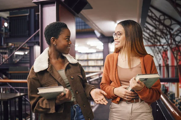 University students, library and talking about books, education and learning together at campus. Women friends have conversation about knowledge, studying and walking to research studying scholarship.