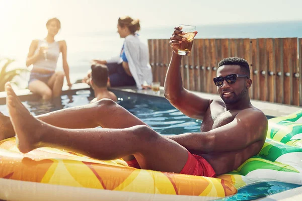 The coolest guy at the party. Portrait of handsome young man raising up his glass for a toast while relaxing in a pool outdoors with friends