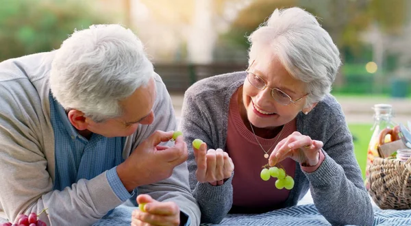 Sharing is caring. a cheerful elderly couple eating grapes together outside in a park