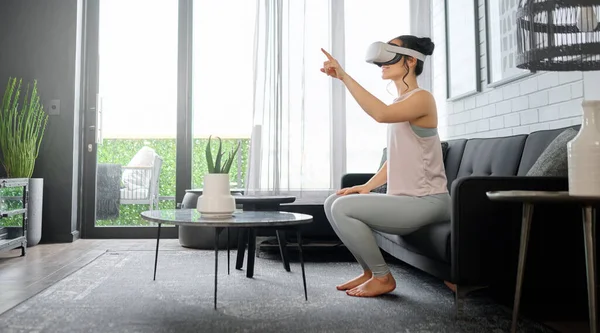 VR, metaverse and gaming with a woman in the living room of her home using a headset to access a 3d game. Futuristic, virtual reality and technology with a female gamer using ai to play games.