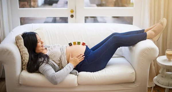 Making sure this is a stressless pregnancy. an attractive young pregnant woman balancing wooden blocks on her tummy while relaxing on the sofa at home