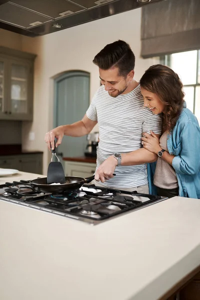 How are you so good at this. a young woman embracing her partner while he cooks breakfast