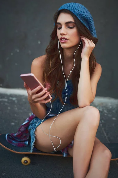 Lets check out the playlist. a carefree young woman seated on the floor while listening to music through her earphones outside during the day