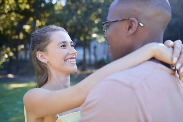 Interracial couple, smile and hug for romantic love, care or embracing relationship in a nature park. Happy black man hugging woman and smiling in happiness for romance, embrace or support outside.