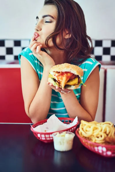 Thats one tasty burger. an attractive young woman enjoying a burger in a retro diner