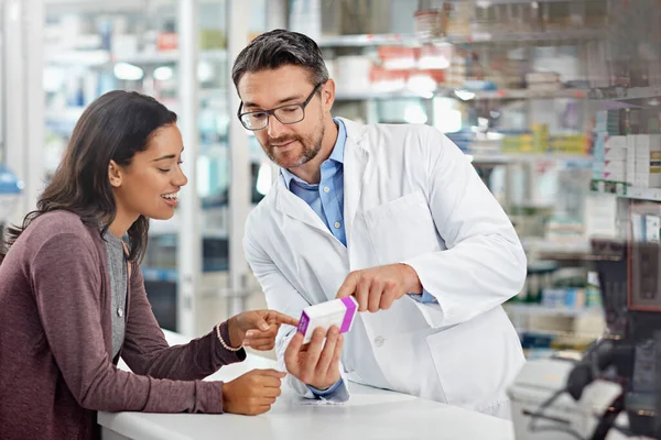 Healthcare service and pharmacy worker with customer at store counter for medication explanation. Pharmaceutical advice and opinion of pharmacist helping girl with medicine information
