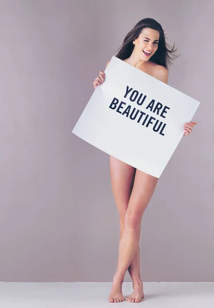 Next time you think of beautiful things, count yourself in. Studio portrait of an attractive young woman holding a sign that reads you are beautiful against a pink background