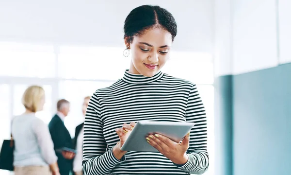 Shes always positive about work. an attractive young businesswoman using a tablet in the office with her colleagues in the background