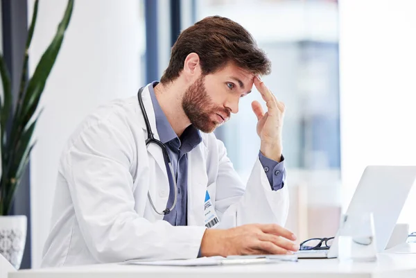 Headache, stress and anxiety of doctor on laptop reading hospital data, results and news fail, mistake or error. Tired, burnout or depression of medical professional with mental health research on pc.