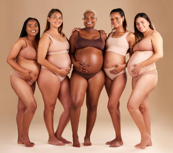 Pregnancy, diversity and portrait of friends in studio for community, motherhood and prenatal wellness. Maternity, love and pregnant women showing their baby bump stomach together by beige background.
