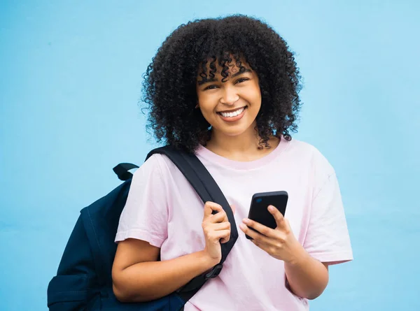 Portrait, student and black woman with bag, phone and tech on blue background. Happy girl, backpack and young person with mobile on social media, educational app or reading online internet connection.
