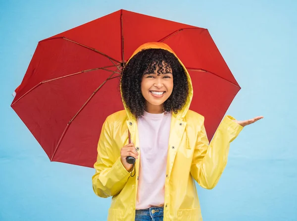Black woman, portrait and rain umbrella and hand checking for drops on isolated blue background in Brazil city. Happy person, student and raincoat for weather protection, rainfall water or insurance.
