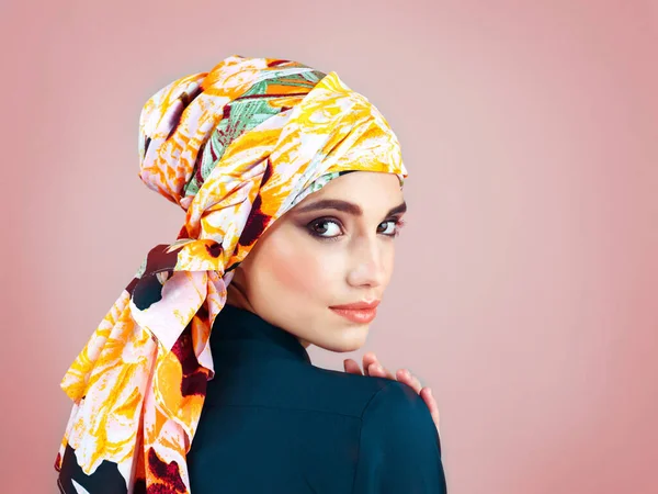 She is one of a kind. Studio portrait of a confident young woman wearing a colorful head scarf while posing against a pink background