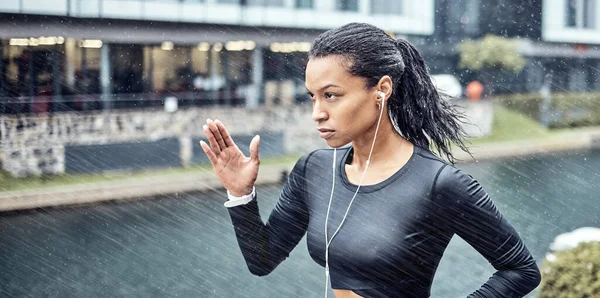黒の女性 フィットネスやスポーツの動機や市内の決意のための雨の中でイヤホンで実行しています アフリカ系アメリカ人のスポーティな女性のランナーは 雨の中で激しいカーディオトレーニングを行う — ストック写真