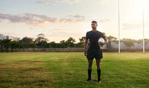 Rugby player, sports and standing on field with ball ready for game, match or practice outdoors. Sporty man athlete or professional waiting for rugby competition, training or play time on green grass.
