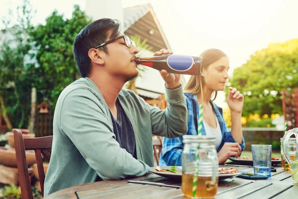 Now that feels good. a young man having a sip of a beer while sitting around a table in an outdoor gathering amongst friends
