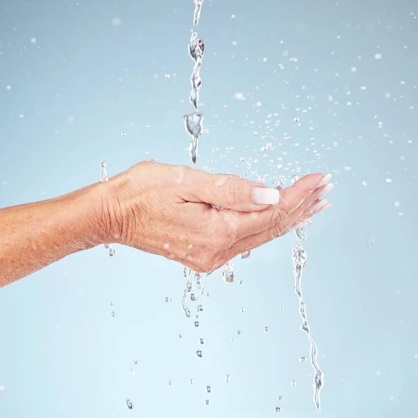 Senior hands, water splash for clean hygiene, fresh sustainability or wash against studio background. Hand of elderly holding natural liquid drops for skin hydration, wellness or safety from bacteria.