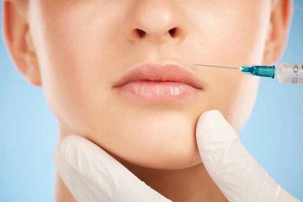 Botox, facial and lip filler by woman with cosmetic injection isolated against a studio blue background. Beauty, beauty and closeup of girl get plastic surgery at a cosmetology clinic using a syringe.