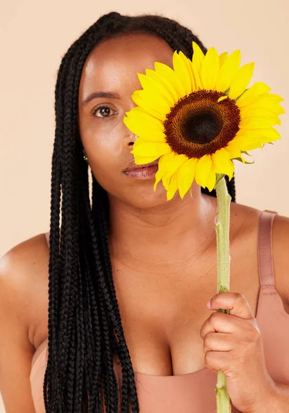 Portrait, beauty and sunflower with a black woman in studio on a beige background for natural treatment or body positivity. Spring, flower and skincare with a young female posing for wellness.