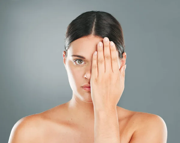 Face, cover and portrait of a woman with a hand on eye isolated on a grey studio background. Skincare, beauty and serious model hiding eyes for dermatology, botox problem and cosmetics on a backdrop.