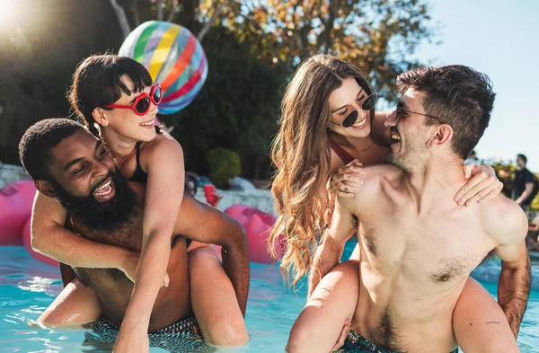 Summer, piggyback and couple of friends in pool for vacation fun and togetherness in the sunshine. Gen z, youth and young people bond, laugh and smile in swimsuit on holiday resort break