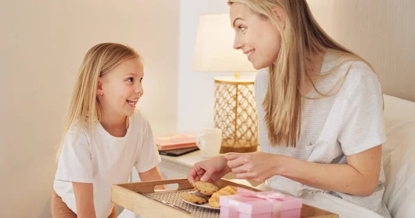 Breakfast, child and mama with a gift on mothers day in the morning to celebrate her mommy at home. Smile, Love and happy girl giving parent a present box and a croissant with cookies in a bedroom.