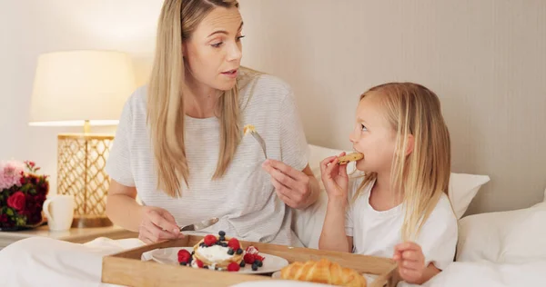 Mother, child and breakfast in the bed of their house together in the morning. Girl relax, calm and in peace while talking and eating food on mothers day with her mom in the bedroom of their home.