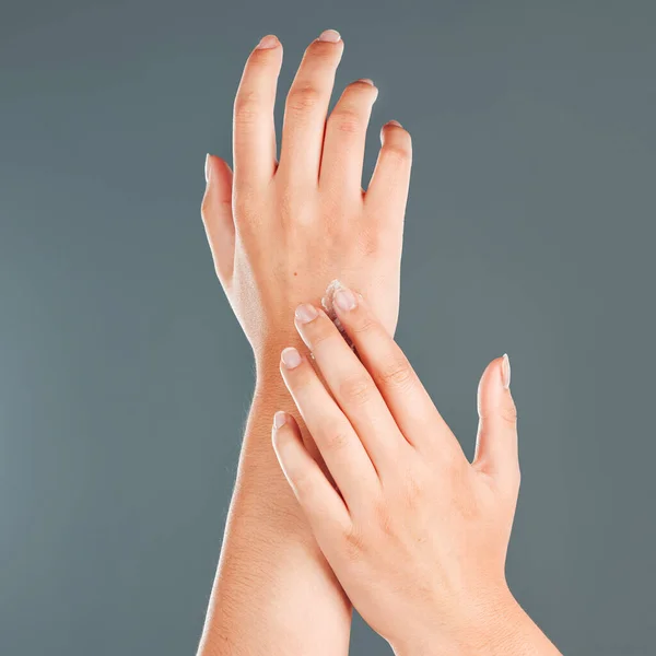 Hands, nail cream and beauty of a woman with moisturizer skincare on arms in studio. Isolated, gray background and person with cosmetic, dermatology and spa lotion for skin and female body glow.