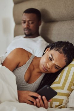 Couple in bed, black woman with smartphone and nosy man, cheating and suspicion for affair, unfaithful and infidelity. Partners in bedroom, male and female with cellphone, chatting and jealous guy. clipart