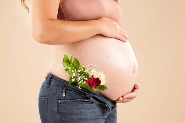 Pregnant woman, rose flowers and stomach in studio for body, maternity wellness and ivf healthcare. Closeup abdomen, floral plants and pregnancy of mother for baby belly, gynecology and natural birth.