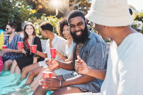 Vacation, drinks and friends speaking in a pool at a summer party, celebration or event at a home. Diversity, happy and people talking, having fun and bonding by the swimming pool while drinking