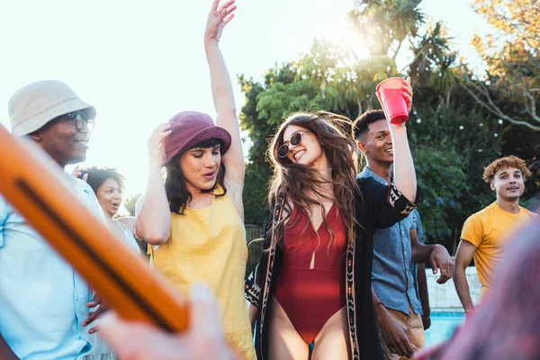 Pool party, drinks and group of friends outdoor to celebrate at festival, location or summer social event. Diversity young men and women people together while dancing, happy and drinking alcohol.