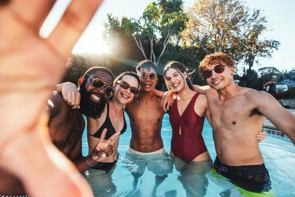 Selfie, peace sign and friends at pool party having fun partying on new year. Swimming celebration, water event and group portrait of people with hand gesture, laughing and taking social media photo.