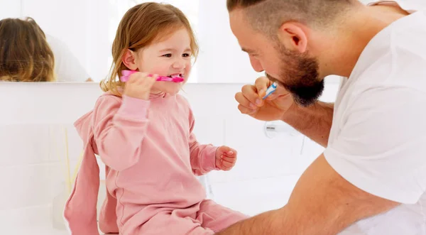 Father and child brushing their teeth with toothbrush together in bathroom of their home. Happy, dental care and man teaching his girl kid oral hygiene routine with toothpaste for health and wellness.