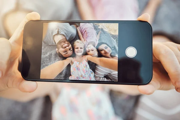 Phone screen, hands and family selfie portrait of hand with mobile zoom and smile on ground. Children, parents and happy together with love and care using a cellphone photo with kids on holiday.