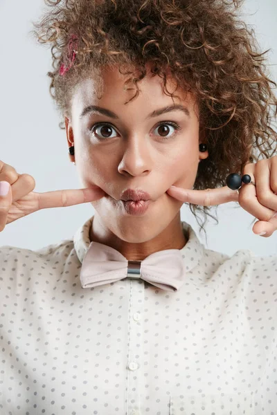 Silly, goofy and portrait of woman in studio with fingers in her cheeks for funny face expression. Fashion, funky and female model with a edgy and stylish bow tie outfit isolated by white background