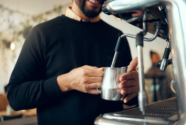 Hands, barista and brewing coffee in kitchen using machine for hot beverage, caffeine or steam. Hand of employee male steaming milk in metal jug for premium grade drink or self service at cafe.