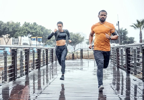 Personal trainer, rain and athletes running as exercise on a city bridge training, fitness or workout outdoors in town. People or fit friends sprint fast for wellness, cardio and health lifestyle.
